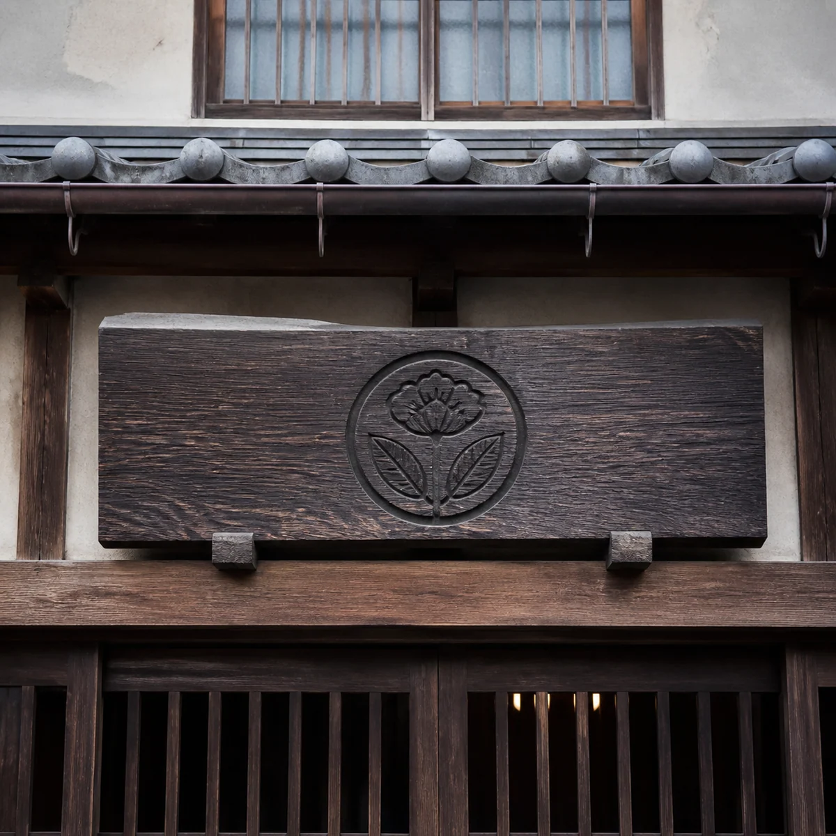 町家の軒下に掛けた、花の紋を彫った木の看板
